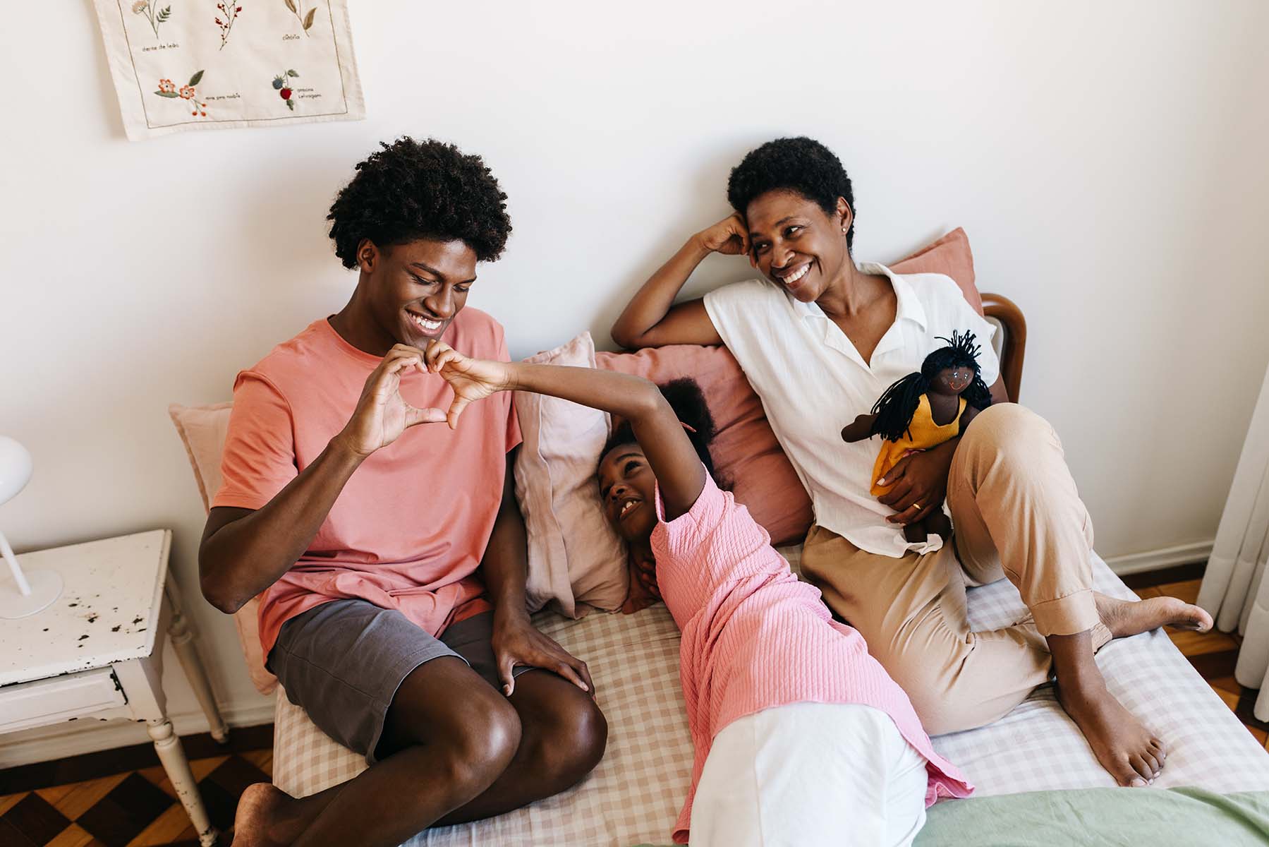 A family forms a heart shape with their hands, smiling on a bed