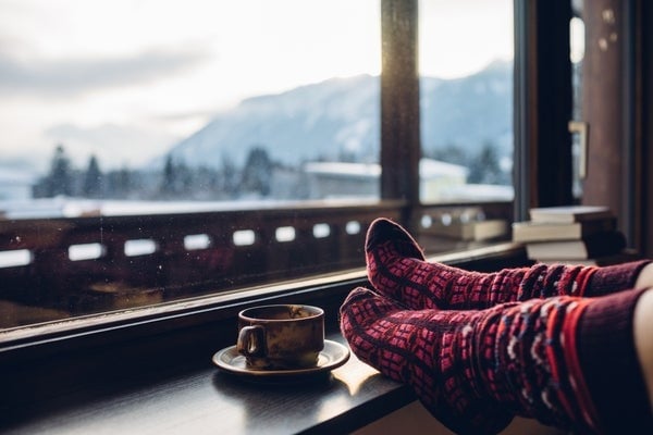 A person wearing holiday-themed socks near a window, which looks out on a snowy scene