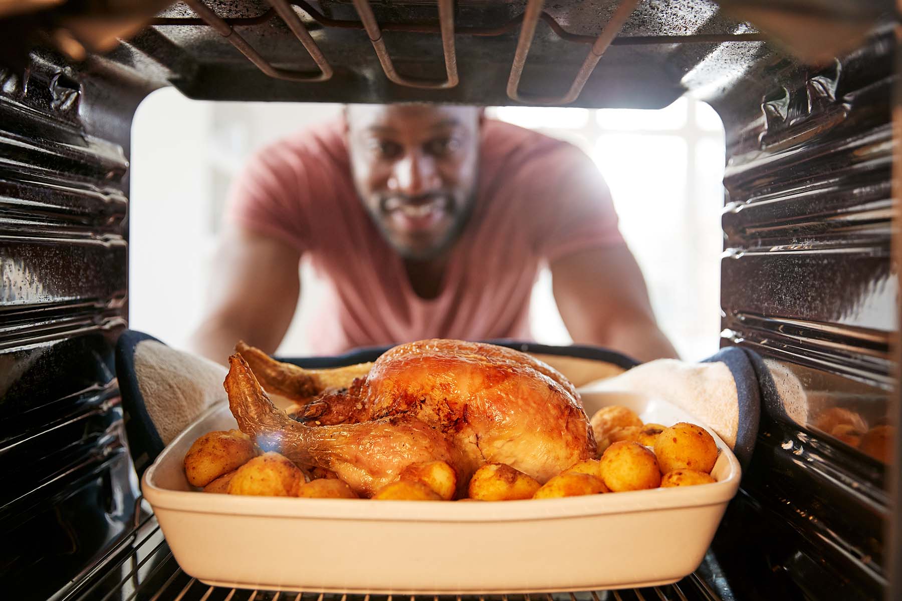 A man smiles as he takes a roasted chicken out of the oven