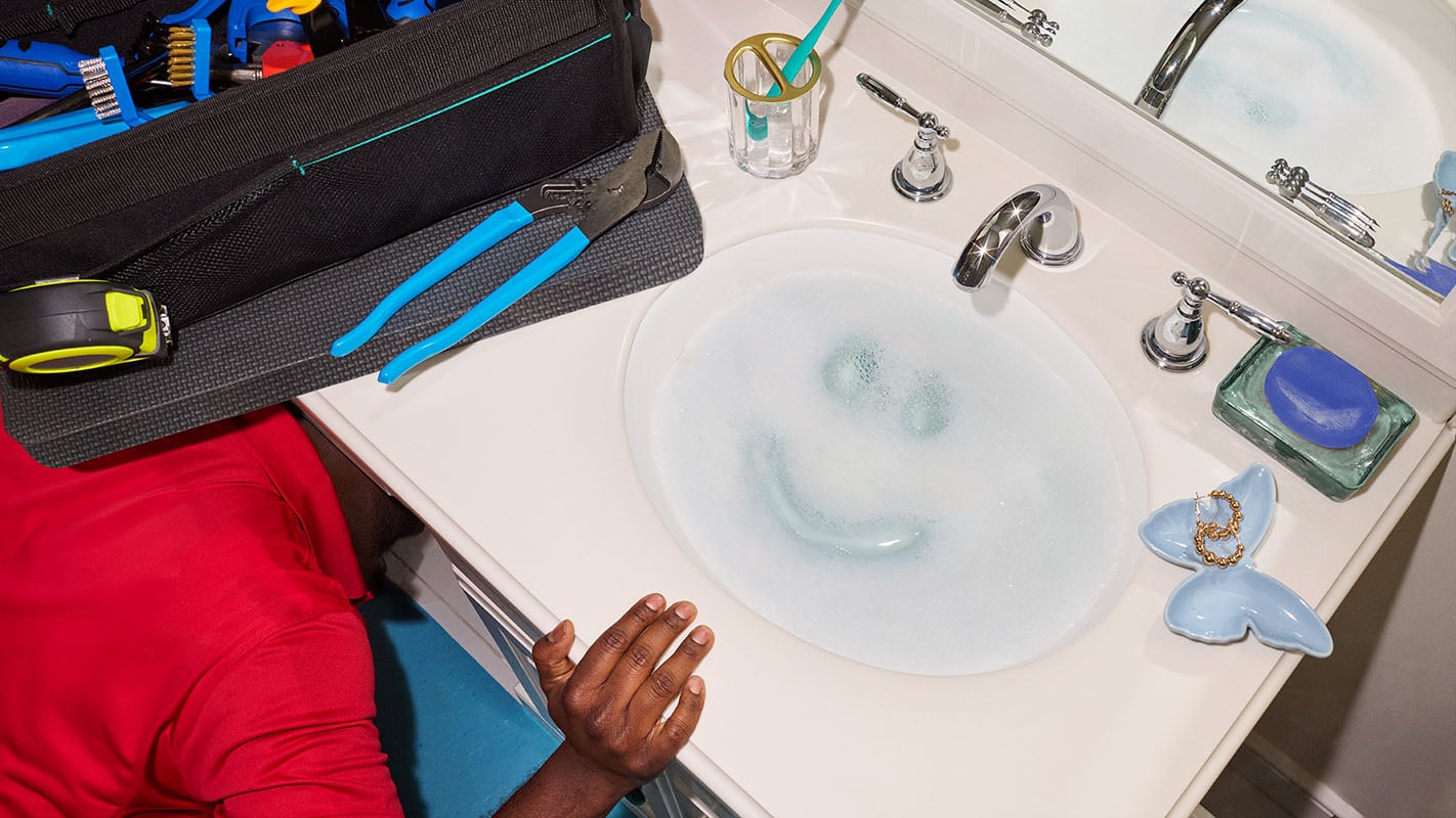 A sink with foaming bubbles and a man working underneath it.