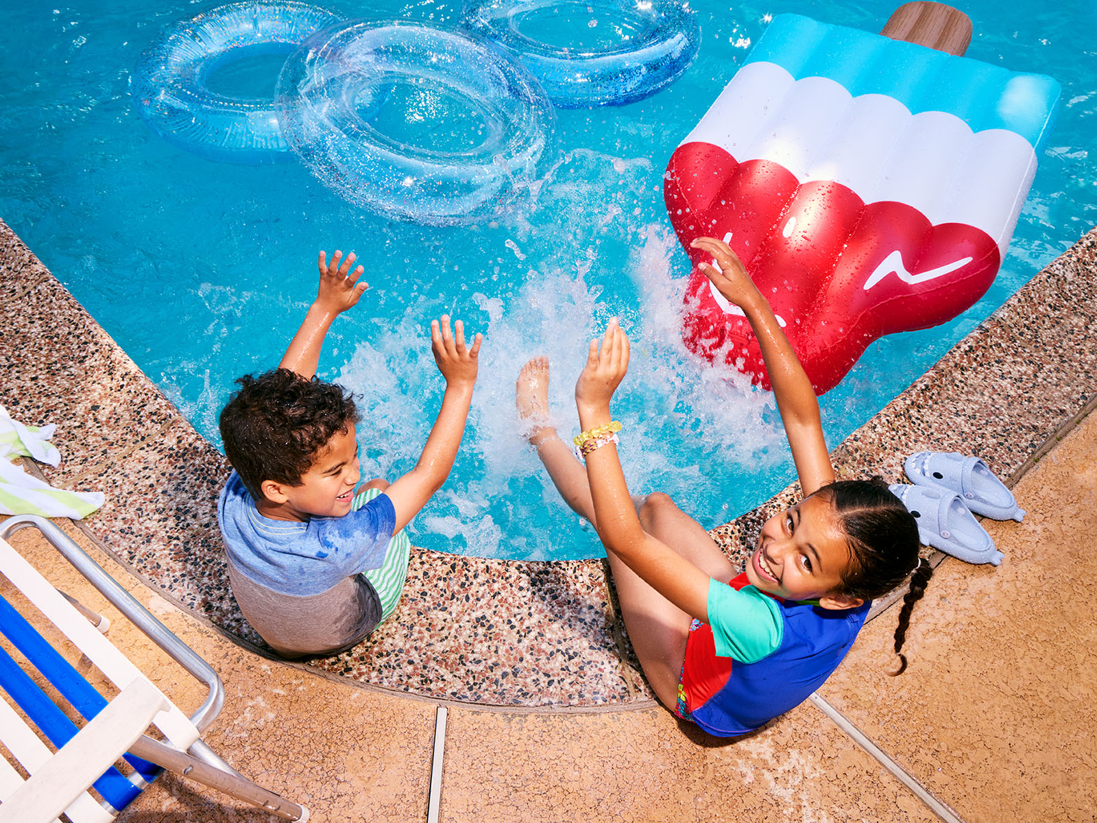 A laughing woman wraps a child in a towel poolside