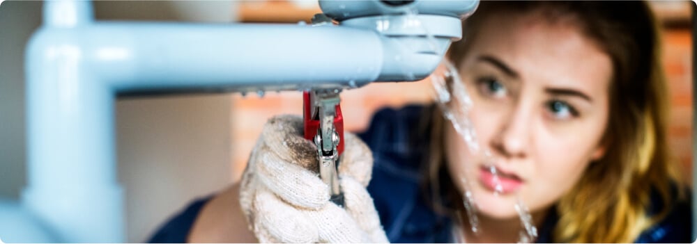 Woman adjusting pipe with wrench.