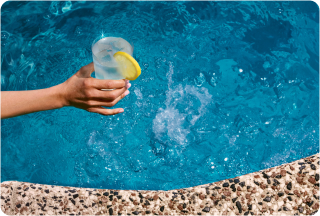 Person holding drink by pool