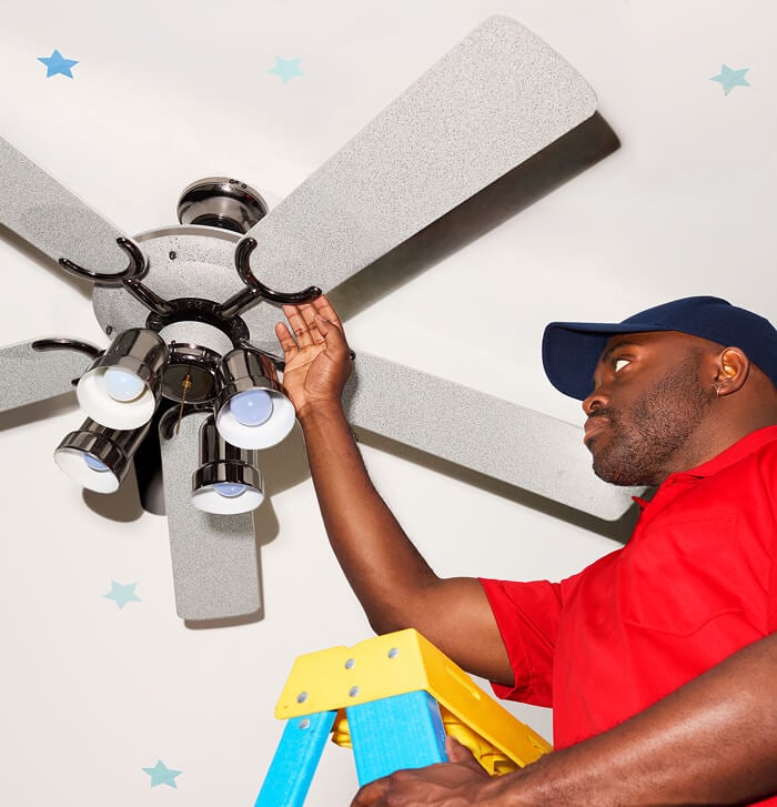 A man wearing a bright red shirt installing a ceiling fan.